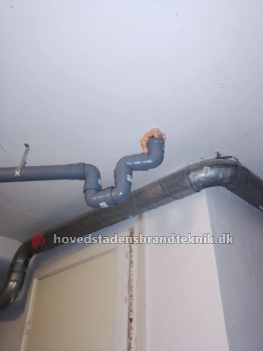 PVC-afløbsrør ført gennem loftet i en kælder uden brandmanchet