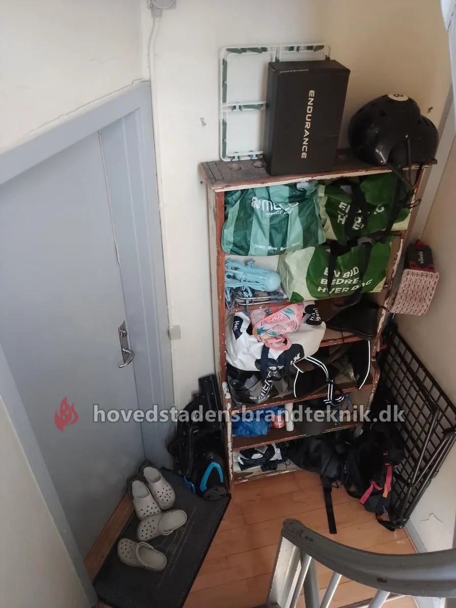 Reol med indkøbsposer, sko og tasker ved en dør på bagtrappen